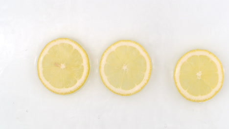 On-a-white-background-a-splash-of-water-falls-on-three-slices-of-lemon-in-slow-motion.